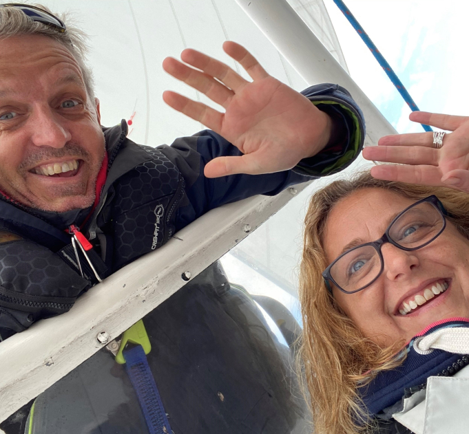 Headshots of Robert and Nicola together waving and smiling with the sail of a yacht above them