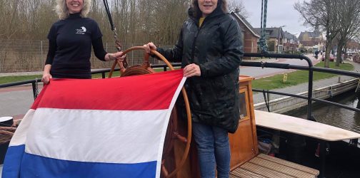 Judith and Thea pose in the cockpit of the SV Poseidon Dutch sailing barge holding a large Dutch flag