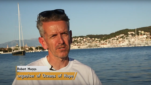 Headshot of Robert standing in front of the sea and a Mediterranean town in the background