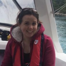 Diane wears a red Oceans of Hope hoodie and is smiling under the canopy of a yacht