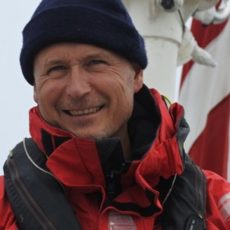 Headshot of Mikkel with a red sailing jacket and dark blue life jacket and beanie hat