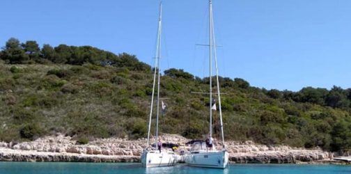 Photo of two yachts rafted up together in front of a beautiful green island with blue skies in the background