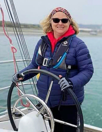 Photo of Nicola at the helm of a yacht wearing a blue sailing jacket and sunglasses